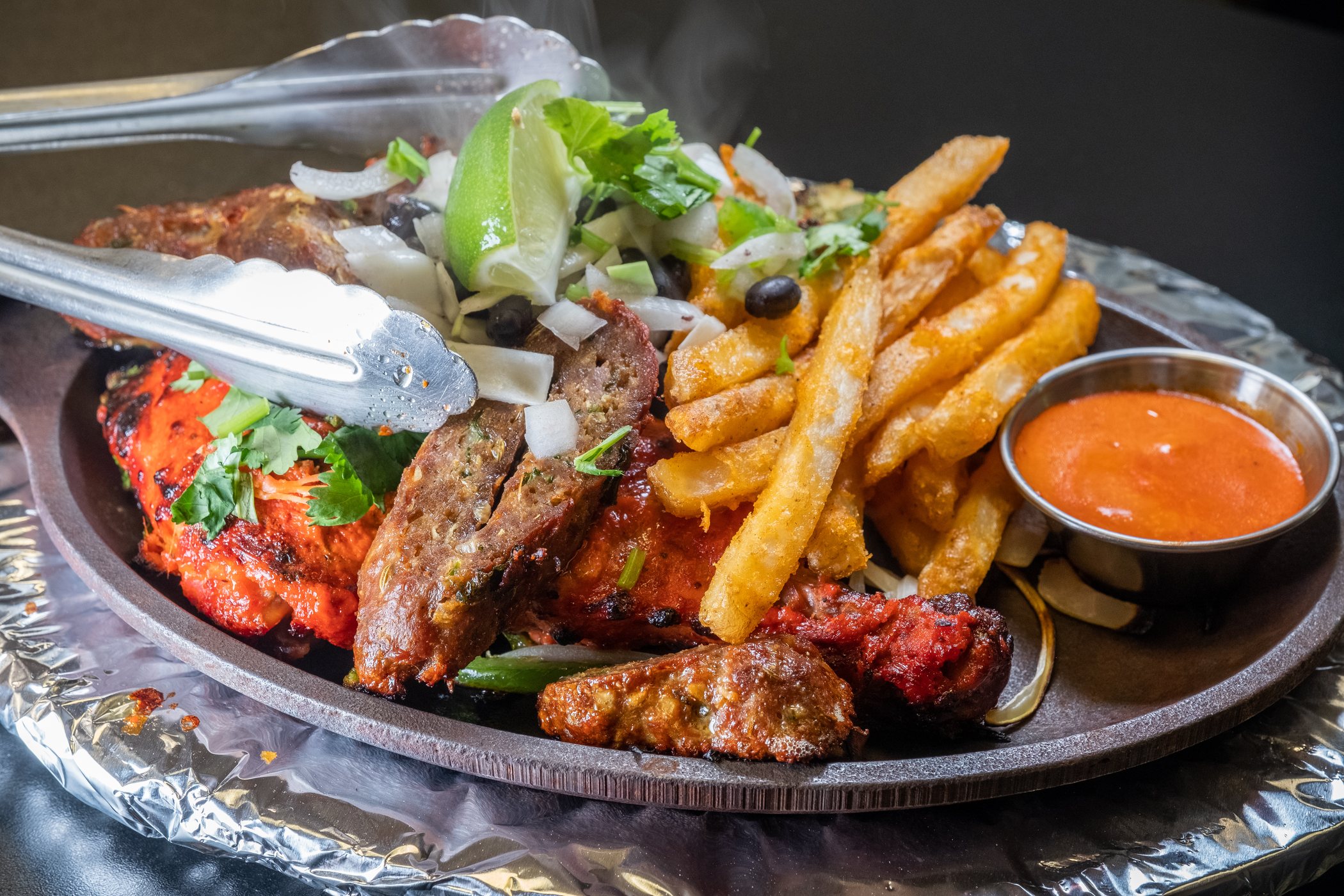 Steaming mixed grill platter with fries, vegetables, lime, and sauces