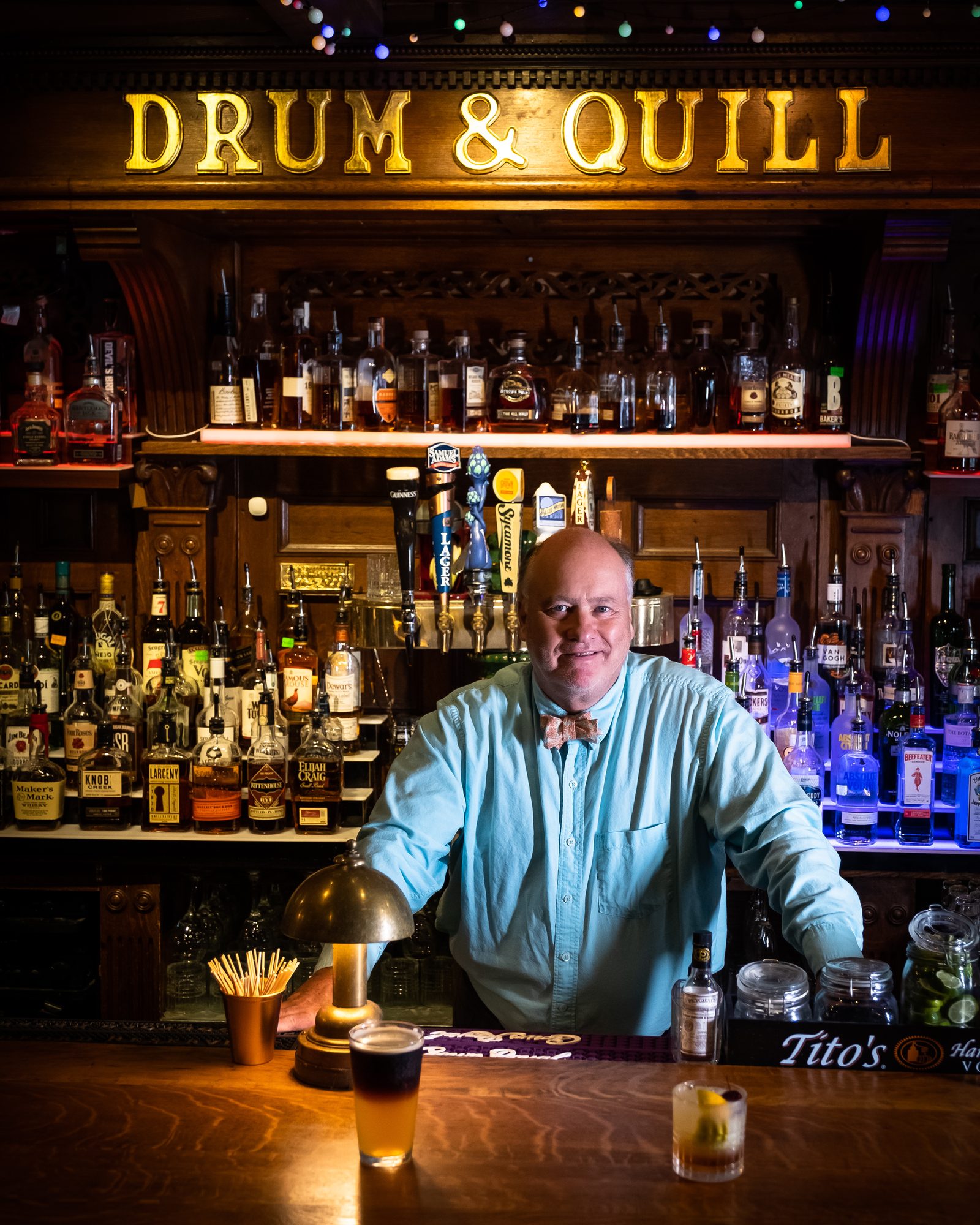Man standing behind a warmly illuminated bar lined with bottles