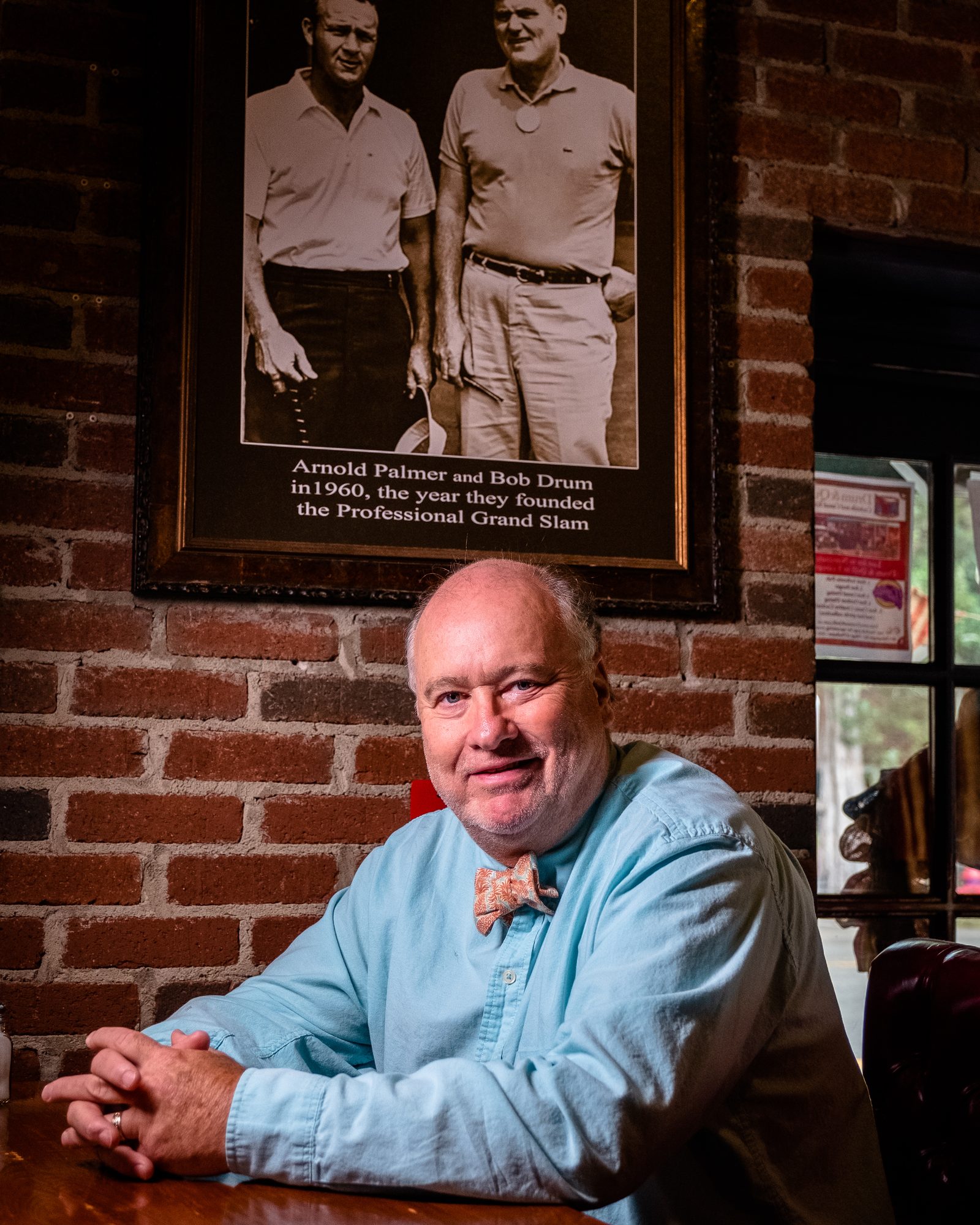 Man seated at a wooden table in a warmly lit brick-walled pub