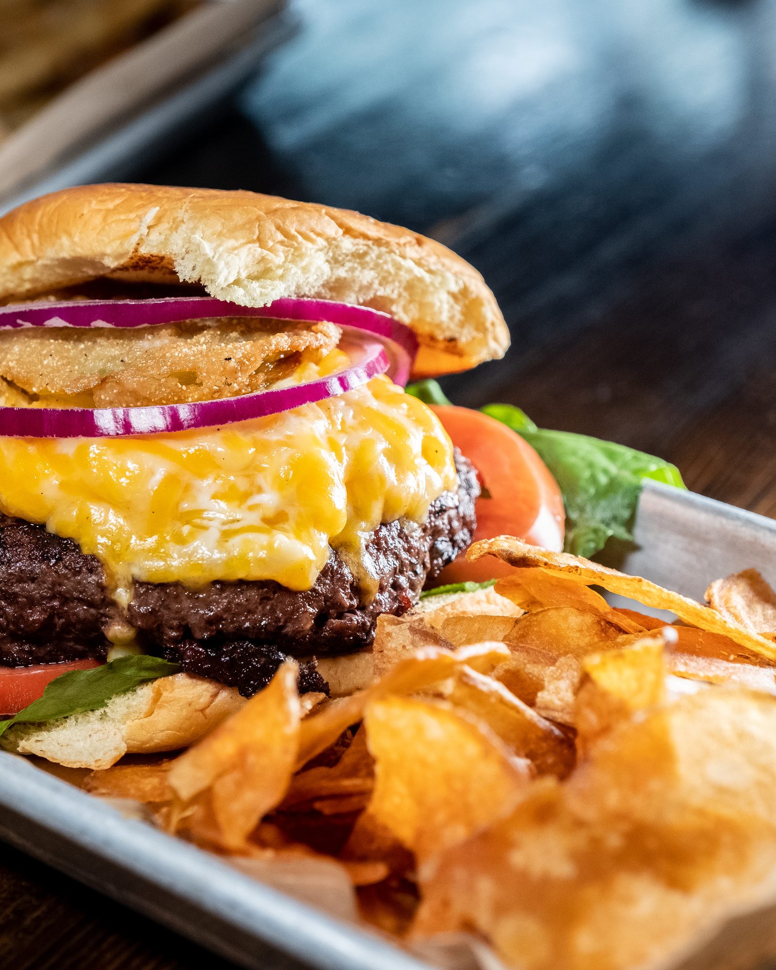 Cheeseburger with red onion and tomato served beside crisp chips