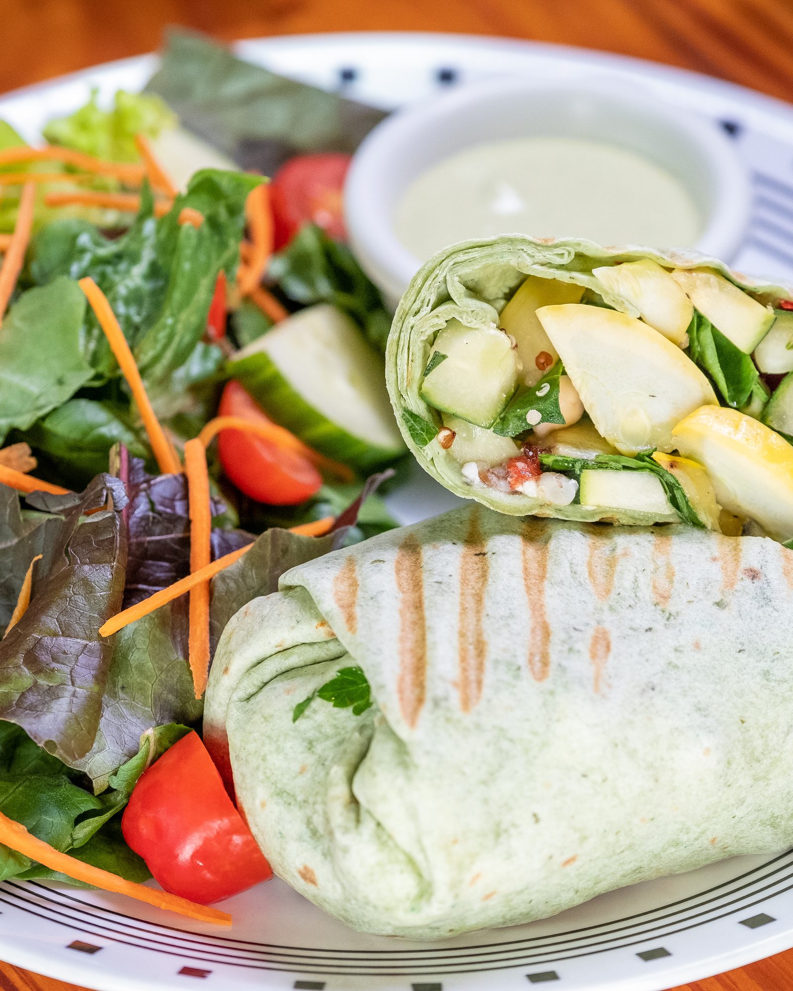 Grilled wrap plated with mixed greens, cucumber ribbons, and two sauces