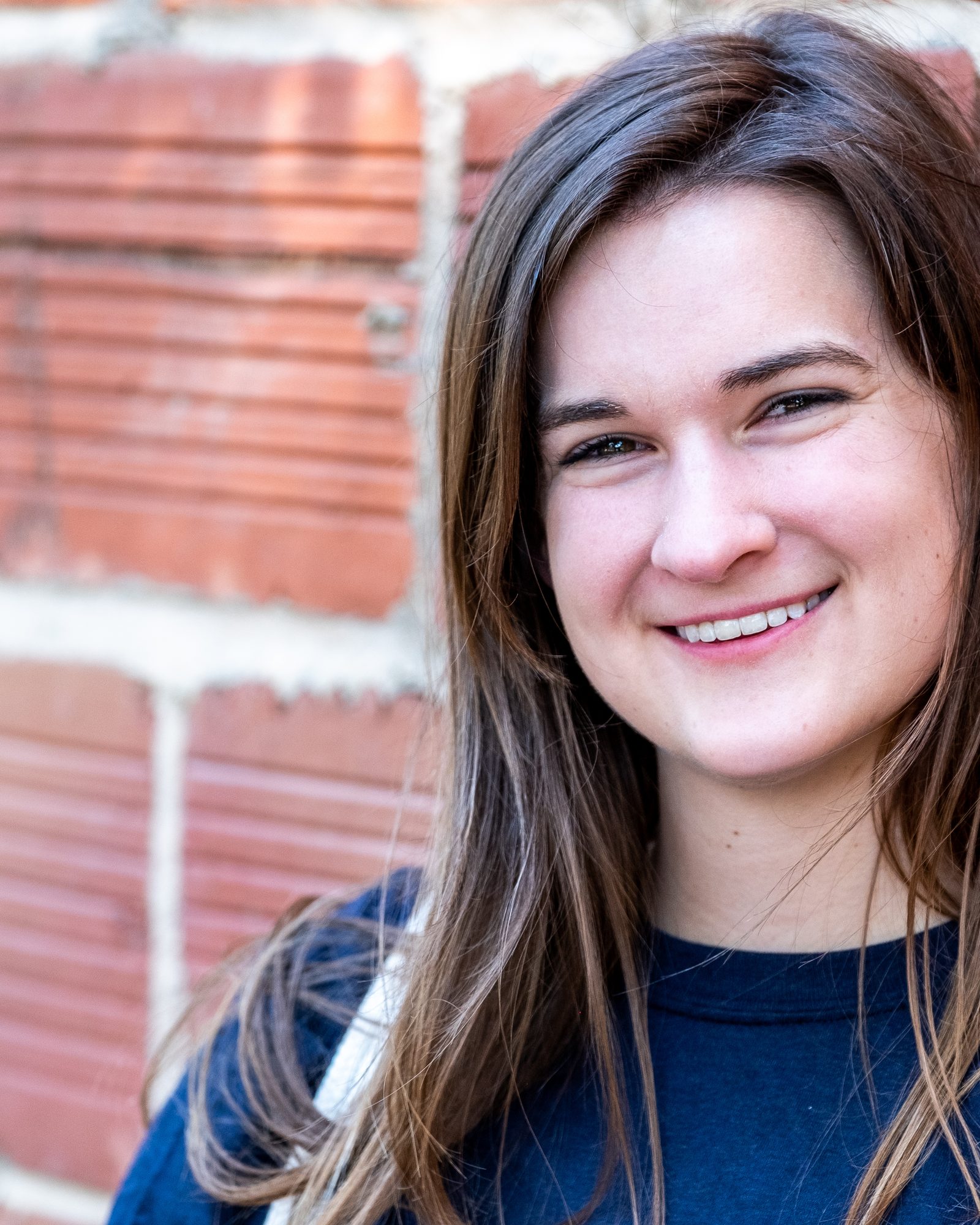 Smiling young woman photographed against warm brickwork