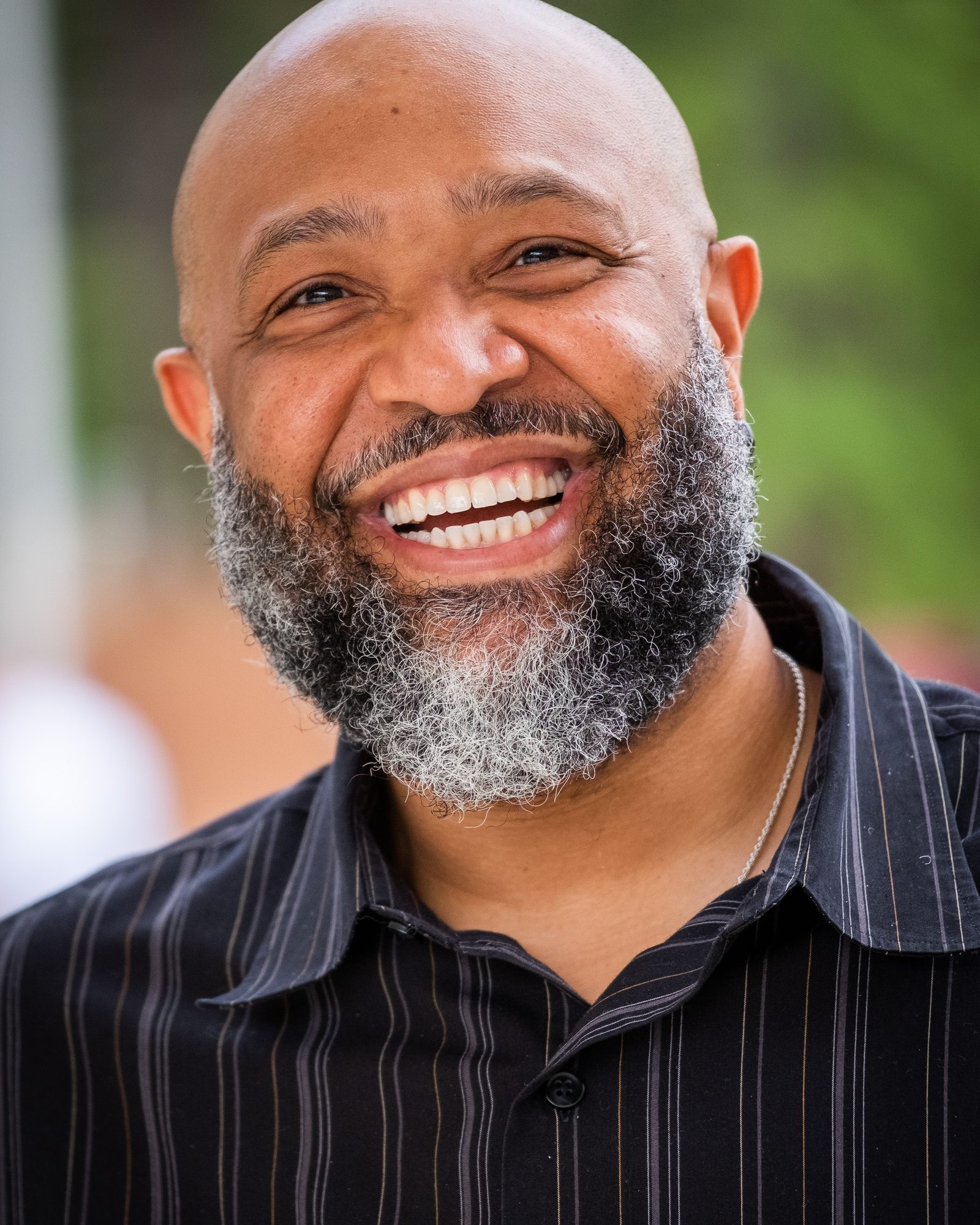 Smiling man photographed outdoors against a softly blurred background