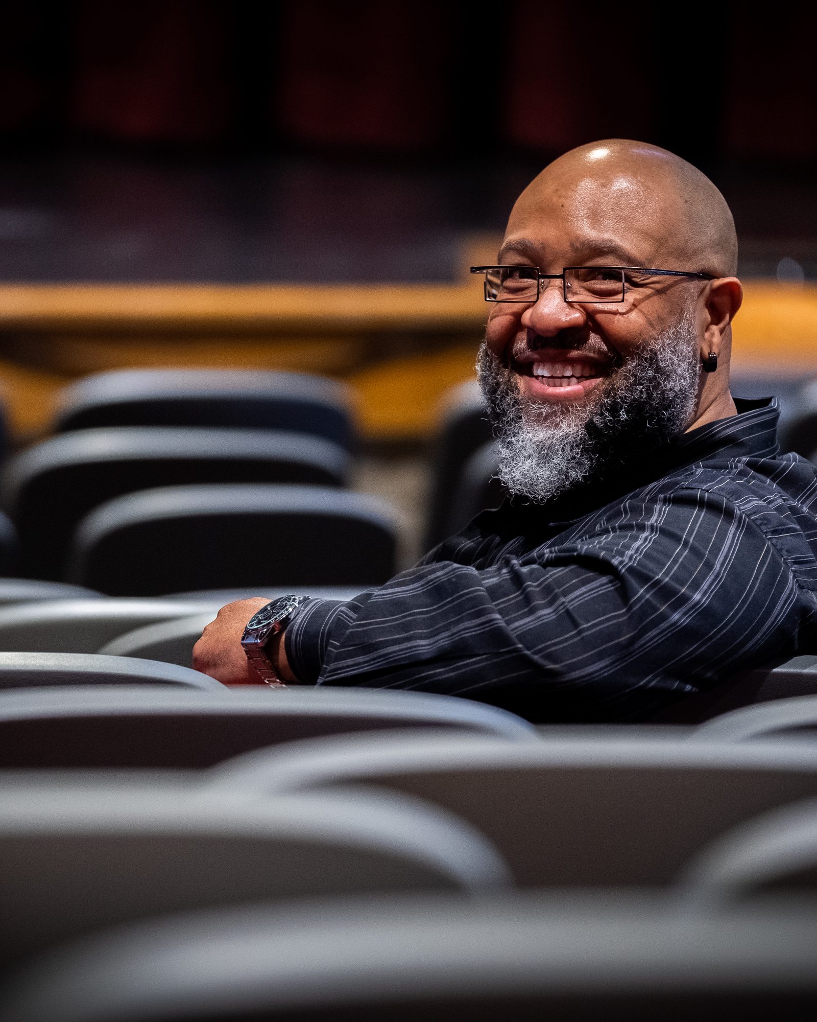 Smiling man photographed among softly blurred theatre seats