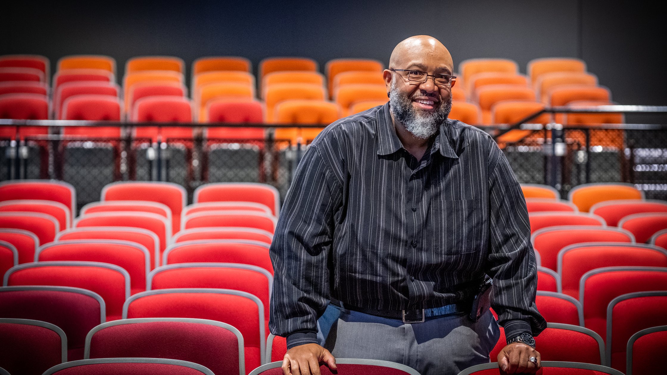 Smiling man standing among vivid red and orange theatre seats