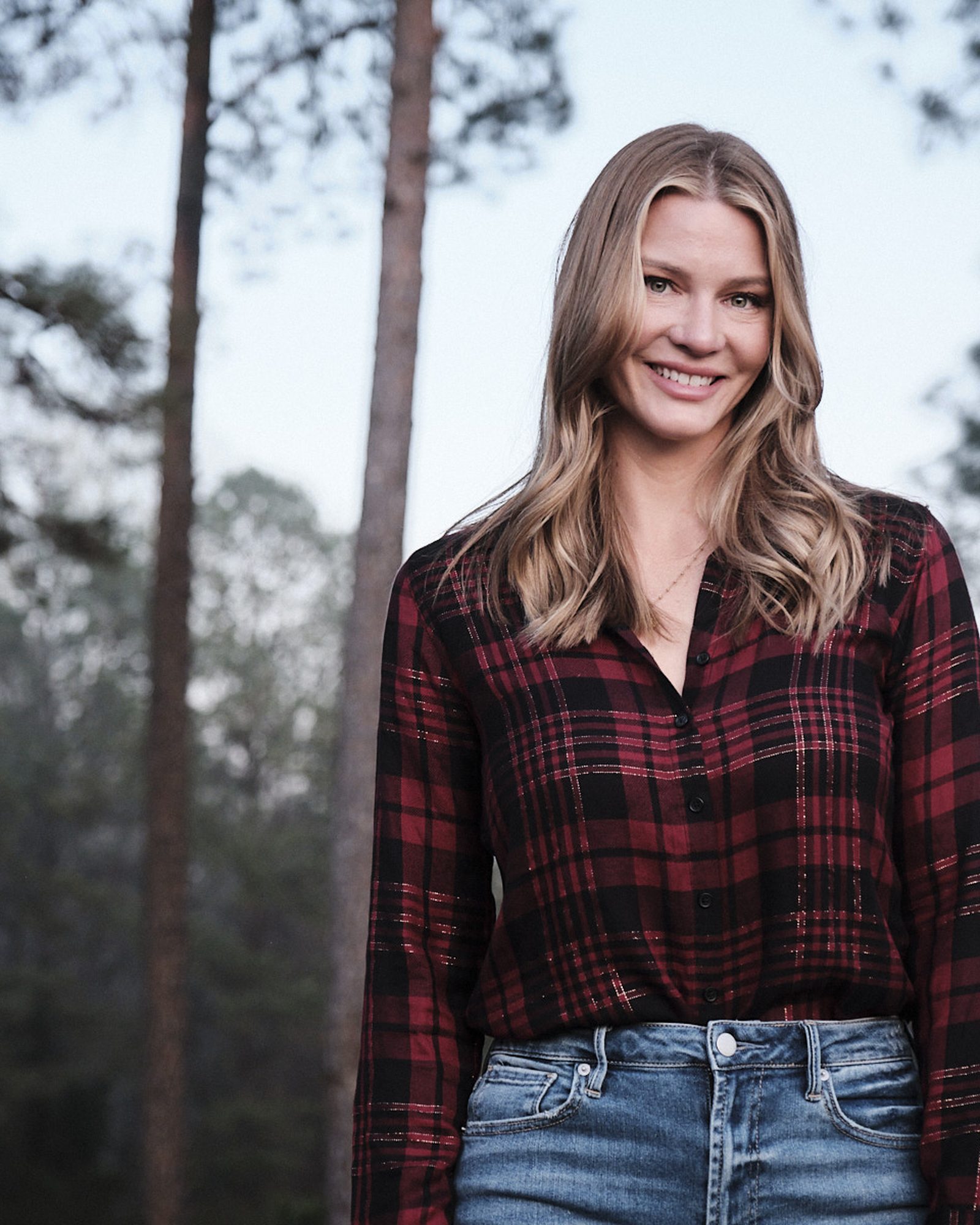 Woman in a plaid shirt photographed among tall pine trees