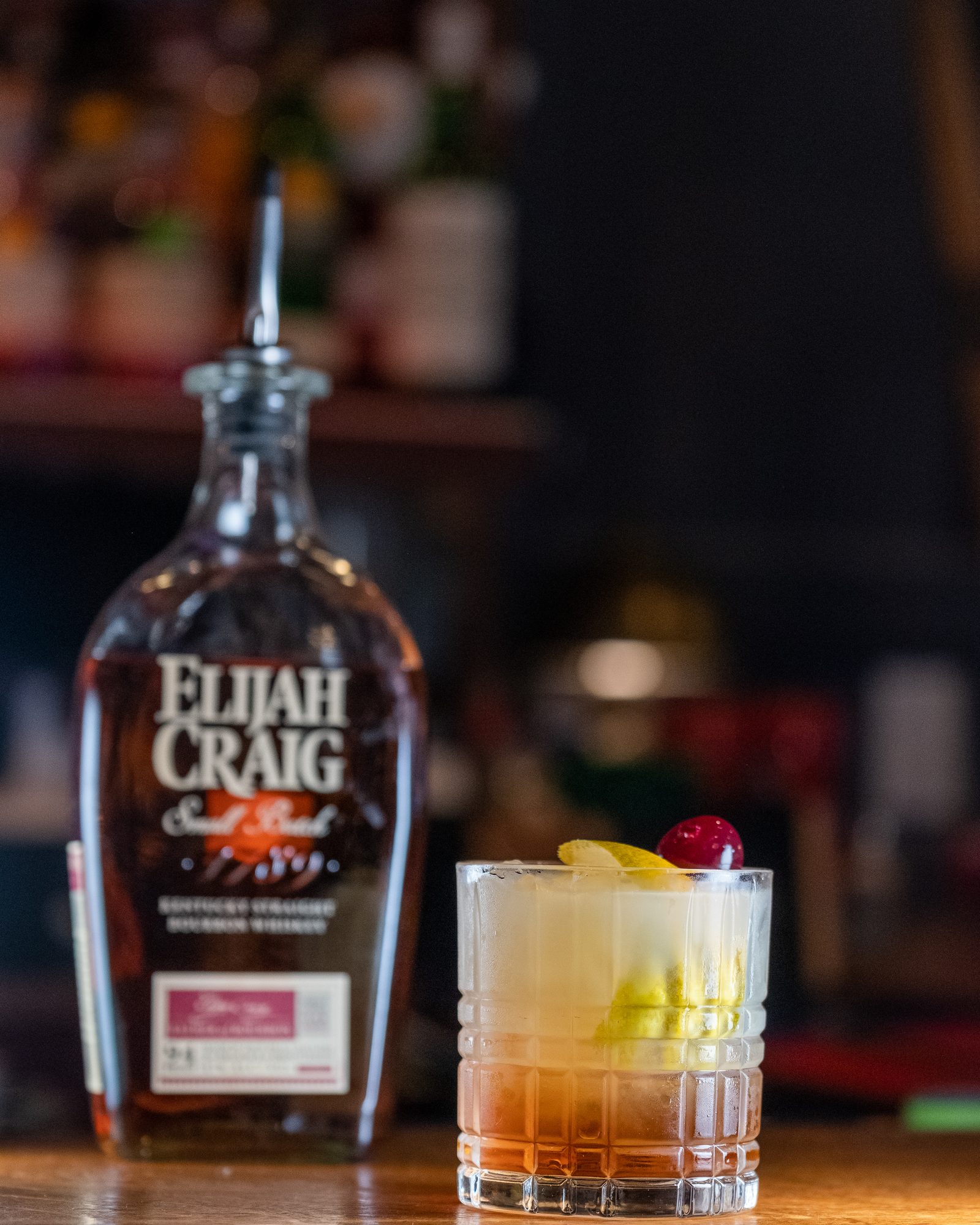 Whiskey bottle and cocktail photographed on a polished bar